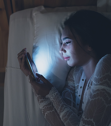 Meisje ligt in bed en kijkt op haar telefoon terwijl het verder donker is.
