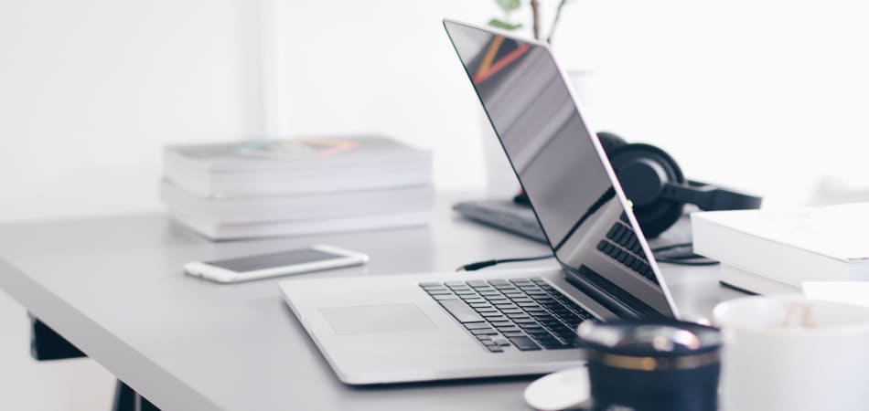 Laptop die half dichtgeklapt op een bureau staat, met daarbij een smartphone en koptelefoon