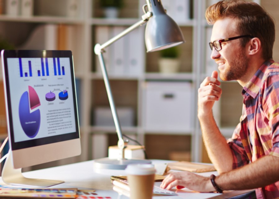Man die, zittend aan een bureau, aan het werk is op zijn computer