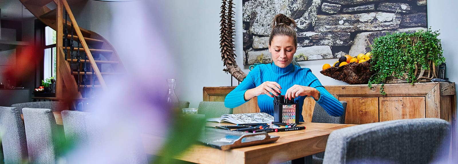 Vrouw zit aan tafel en pakt kleurpotloden. Met de Alles in een Polis heeft u 1 pakket voor al uw schadeverzekeringen.