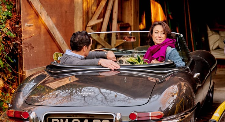 Man en vrouw zitten in oldtimer en rijden weg vanuit de garage.