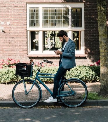 Een man zit op zijn fiets en staat met 1 been op de stoep met een telefoon in zijn hand