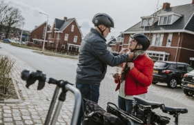 Man en vrouw staan voor e-bikes en zetten fietshelmen op.
