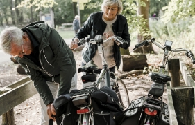 Een man buigt iets omlaag om een fietstas vast te maken. Aan de accu is te zien dat hij een elektrische fiets heeft.