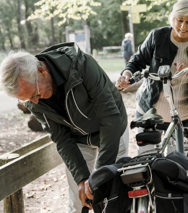 Een man buigt iets omlaag om een fietstas vast te maken. Aan de accu is te zien dat hij een elektrische fiets heeft.