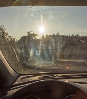 man die aan het autorijden is terwijl de zon die op de voorruit schijnt