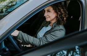 Een vrouw zit achter het stuur van een stilstaande auto, met het portier open