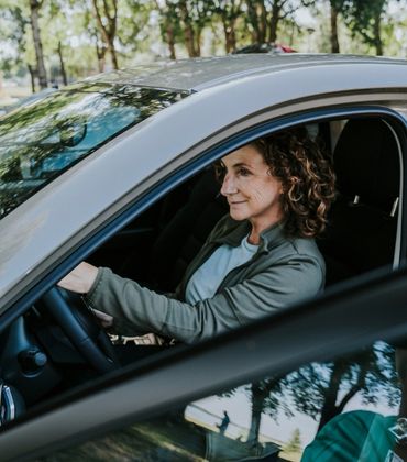 Een vrouw zit achter het stuur van een stilstaande auto, met het portier open