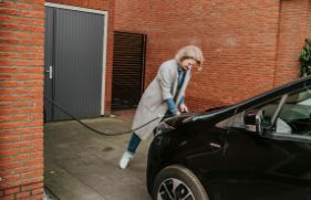 Een vrouw steekt de stekker van de laadkabel in de voorkant van haar elektrische auto.