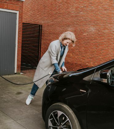 Een vrouw steekt de stekker van de laadkabel in de voorkant van haar elektrische auto.