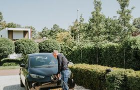Een man steekt de stekker in de voorkant van zijn elektrische auto.