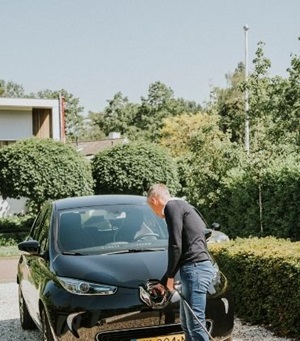Een man steekt de stekker in de voorkant van zijn elektrische auto.
