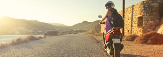 Een toerist die wegrijdt op een scooter en achterom kijkt