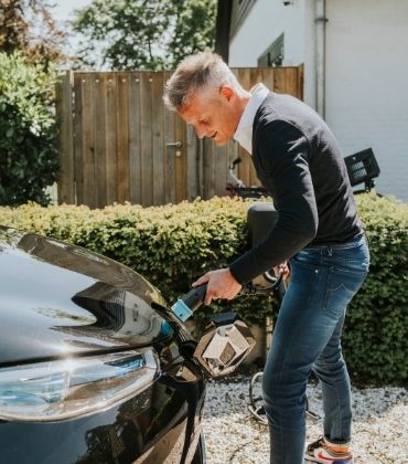 Man steekt de oplaadkabel in zijn elektrische auto