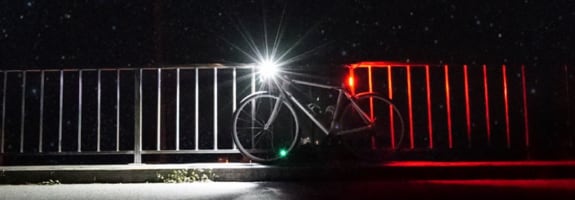 Een fiets met brandend voorlicht en achterlicht die tegen een hek aanstaat