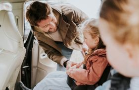 Een vader doet de veiligheidsgordel om bij zijn dochter, die in de auto zit. 