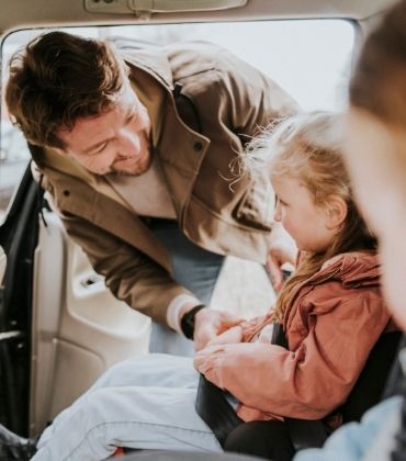 Een vader doet de veiligheidsgordel om bij zijn dochter, die in de auto zit. 