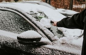 Iemand haalt met een ijskrabber sneeuw van de vooruit van een auto