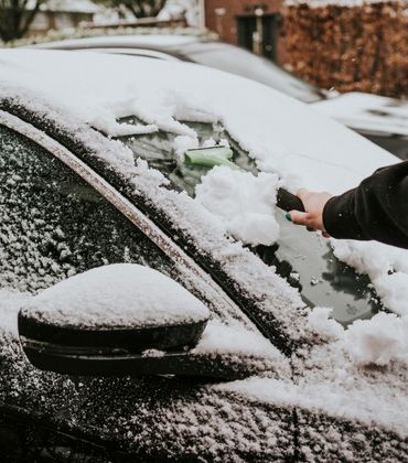 Iemand haalt met een ijskrabber sneeuw van de vooruit van een auto