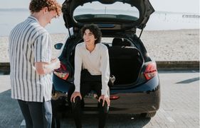 Jongen zit in de kofferbak van een auto dichtbij het strand staat geparkeerd. Een andere jongen staat ernaast. Samen lachen ze.