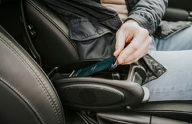 Iemand zit in de auto met de hand aan een telefoon die in de midden console ligt