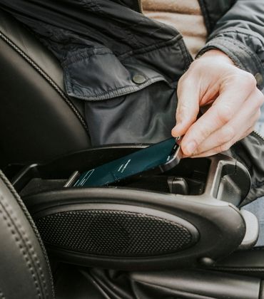 Iemand zit in de auto met de hand aan een telefoon die in de midden console ligt