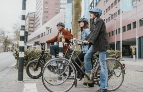 3 jongeren op hun fiets met een fietshelm op wachten voor een stoplicht.