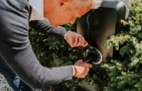 Een persoon steekt de stekker van een elektrische auto in een oplaadpunt. 