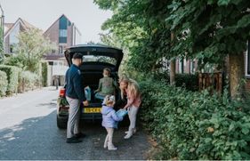 Een gezin staat bij de auto met spullen achterin en de achtklep van de auto is opengeklapt