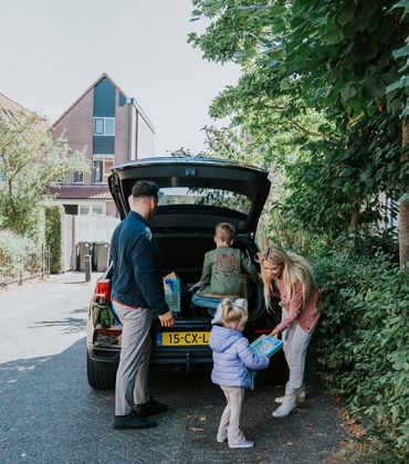 Een gezin staat bij de auto met spullen achterin en de achtklep van de auto is opengeklapt