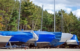 Een rij met boten die op land zijn opgeslagen. Over elke boot is een blauw zeil getrokken.