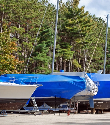 Een rij met boten die op land zijn opgeslagen. Over elke boot is een blauw zeil getrokken.