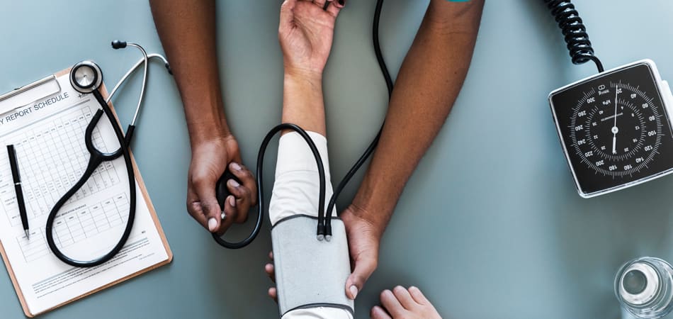 een dokterstafel van bovenaf gezien, waar een arts de bloeddruk van een patiënt opneemt