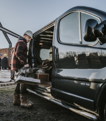 Een man met een bouwhelm op zijn hoofd laadt spullen in een bedrijfswagen.