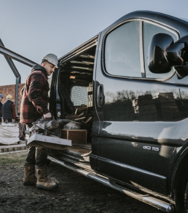 Een man met een bouwhelm op zijn hoofd laadt spullen in een bedrijfswagen.