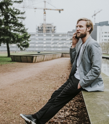 Een man zit te bellen op de rand van een verhoogde vijver in een stadspark.