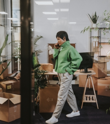 Iemand staat midden in een sfeervolle ruimte met veel planten en natuurlijke kleuren te bellen met een mobiele telefoon.