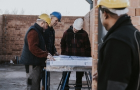 3 mannen staan op een bouwplaats en kijken naar een bouwtekening