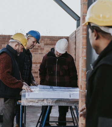 3 mannen staan op een bouwplaats en kijken naar een bouwtekening