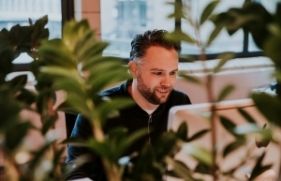 Vriendelijk kijkende man achter laptop met planten op de voorgrond