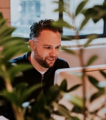 Vriendelijk kijkende man achter laptop met planten op de voorgrond