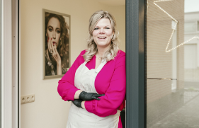 Vrouw staat in de deuropening van haar eigen zaak.