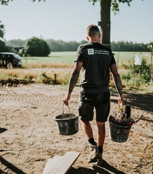 Een man met een shirt van Van Den Bosch metselwerken loopt op een bouwplaats met in iedere hand 1 emmer