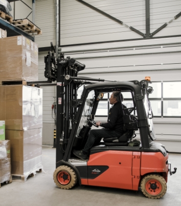 Een persoon gebruikt een heftruck om pallets op elkaar te stapelen.