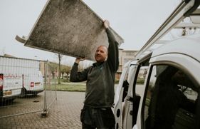 Een man tilt een onderdeel van een rolsteiger uit zijn bedrijfsauto.