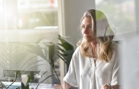 Vrouw met lang blond haar zit achter een beeldscherm en kijkt serieus