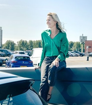 Marjolein Groen, directeur Sustainability en CSR bij mobiliteitsprovider Athlon Nederland, draagt een groene bloes en zit lachend op een parkeerplaats
