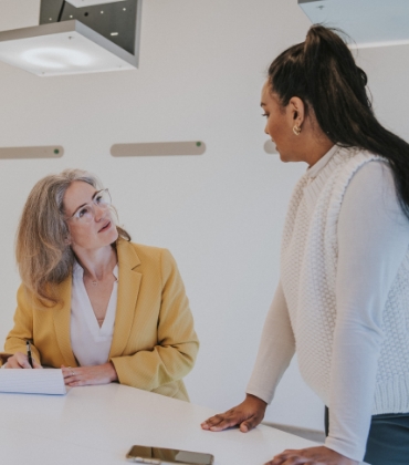 2 vrouwen zijn in gesprek met elkaar in een vergaderruimte. 