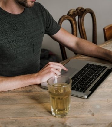 Man in t-shirt zit achter laptop, met een glas thee