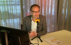 Man met bril zit aan een tafel achter een microfoon